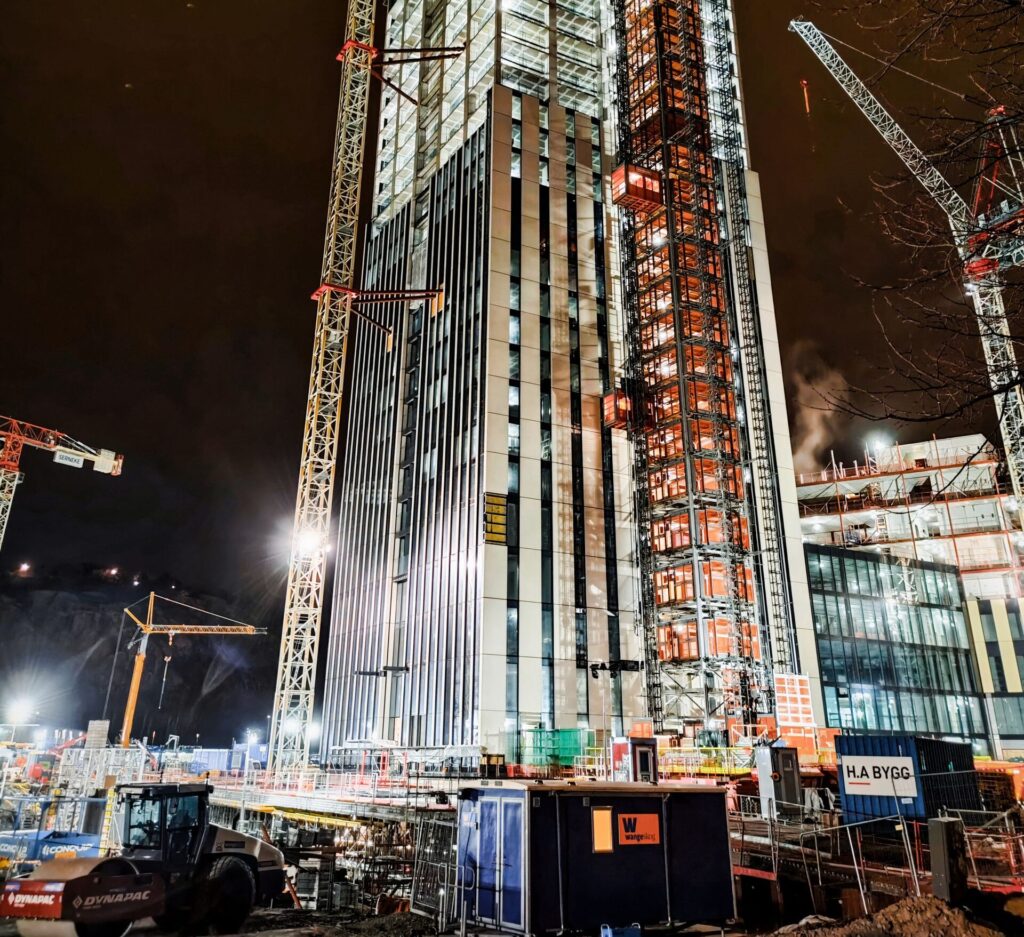A modern skyscraper under construction at night in Lindholmen, Sweden, illuminated by cranes and lights.