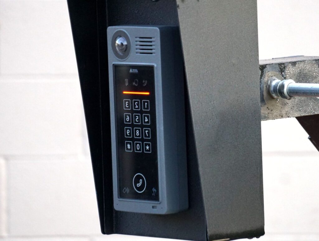 Close-up of a modern security intercom and keypad mounted on a wall outdoors with visible wiring.